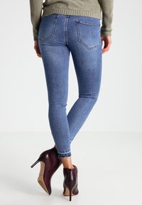 Úzké modré džíny denimového materiálu s pěti kapsami, s mírným ošoupáním na lemu, v kombinaci s vínovými botami na vysokém podpatku.