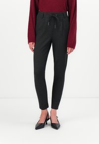Sorte pinstripe bukser med snor i taljen, tætsiddende pasform og glat tekstur, parret med spidse sorte hæle.
