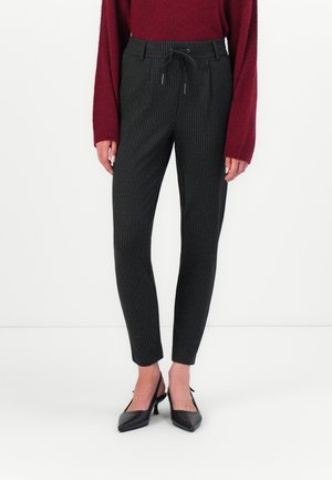 Pantalon noir à rayures fines avec une taille à cordon, coupe slim et texture lisse, associé à des escarpins noirs pointus.