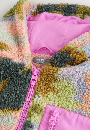 Mehrfarbige, flauschige Jacke mit pinkem Futter, pinken Reißverschlüssen und dem Markenschild "NEXT" im Kragen.