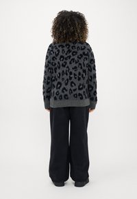 Sweater cinza com um padrão de leopardo preto, punhos e barra canelados, combinado com calças largas pretas e sapatos pretos.