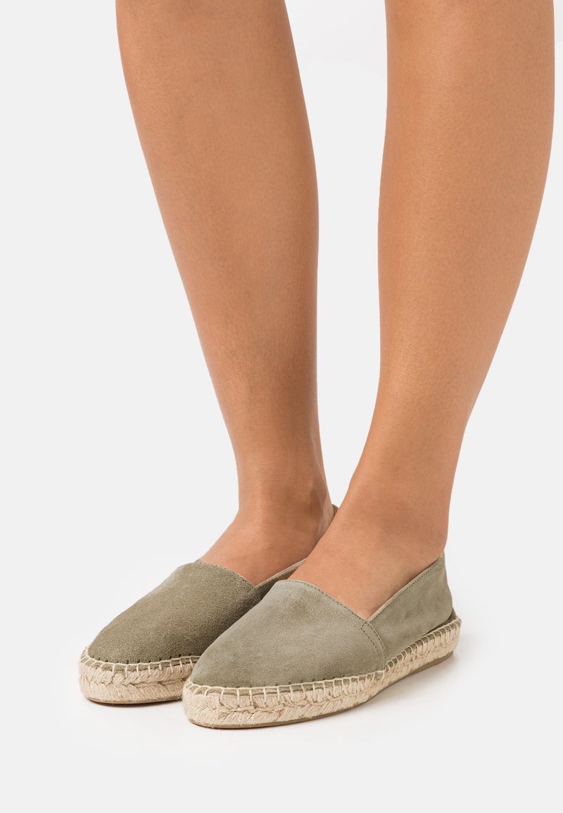 Espadrilles vert olive avec dessus en daim, semelle en corde de jute et détails cousus le long du bord. Conçues pour un enfilage facile.