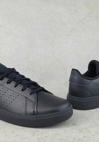 Čierne kožené tenisky s perforovanými bočnými panelmi, okrúhlou špičkou, plochou gumenou podrážkou a zodpovedajúcimi šnúrkami. Logo viditeľné na päte.