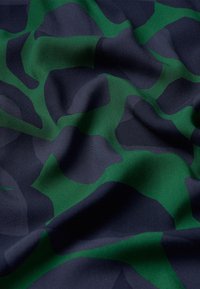 Tessuto testurizzato in blu navy e motivo camouflage verde, con superficie tessile liscia caratterizzata da forme astratte intrecciate e una leggera caduta.
