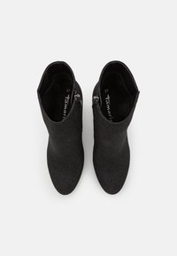 Une paire de bottines noires à chevilles avec des fermetures éclair latérales, des bouts pointus et un tissu texturé, présentée en vue de dessus sur un fond blanc.