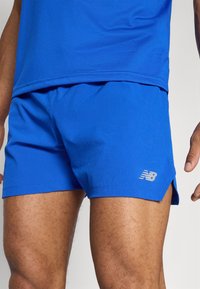 Bermudas atléticas azuis feitas de tecido respirável com textura perfurada, apresentando um pequeno logotipo cinza e fendas laterais para mobilidade.
