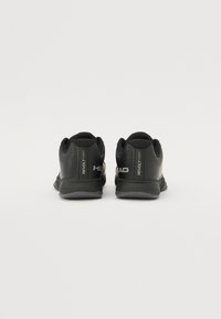 Schwarze Sportschuhe mit Mesh-Obermaterial, strukturierten Seiten und grauer Sohle. Mit Branding "HEAD" und "REVOLT COURT" an der Ferse. Minimalistisches Design.