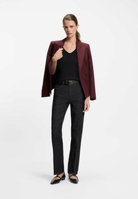 Burgunderfarbener, doppelt geknöpfter Blazer über einem schwarzen, gerippten Oberteil, kombiniert mit dunklen, geraden Hosen und schwarzen flachen Schuhen, die ein schlichtes Design aufweisen.