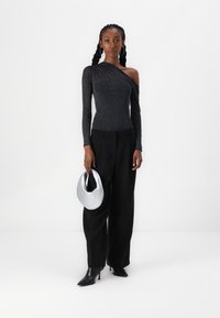Schwarzes, langärmliges Top mit schulterfreiem Design und glitzernder Textur; kombiniert mit hochgeschnittenen schwarzen Hosen und einer silbernen Halbmondtasche.