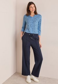 Blauw gestreepte lange mouwen top met ronde hals, gecombineerd met marineblauwe wijde broek met voorzakken en een trekkoord in de taille.