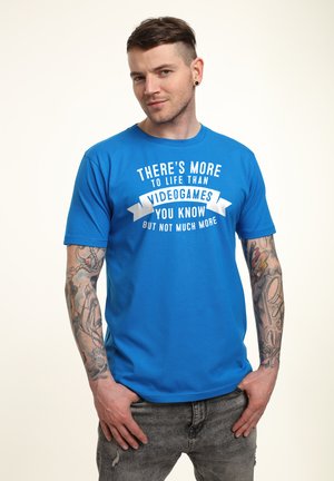 Blå grafisk t-shirt lavet af blødt stof, med hvid tekst på et bannerdesign, der står: "Der er mere til livet end videospil."