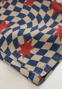 Blue and beige wavy checkerboard pattern fabric with red eight-pointed stars and visible stitching on folded edge.