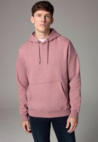 Sudadera con capucha de suave tela rosa, con un bolsillo tipo canguro, cordones y puños acanalados, combinada con jeans oscuros.