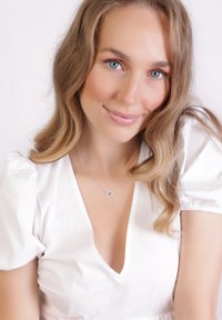 Zilveren ketting met een hartvormige hanger, gedragen door een vrouw in een witte jurk met pofmouwen en een V-hals, met golvend haar.