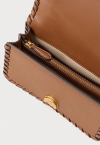 Braune Lederhandtasche mit geflochtenem Rand, goldenen Beschlägen und einem Reißverschlussfach innen. Verfügt über eine glatte Oberfläche und dezente Markenkennzeichnung.