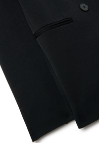Blazer noir avec une texture de tissu lisse, fermeture à un bouton, et un détail de poche discret sur le côté gauche.