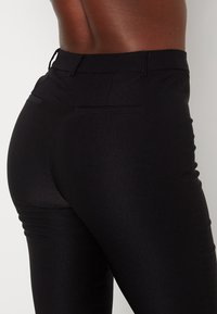 Pantalon ajusté noir avec une texture lisse et extensible. Caractéristiques : taille haute et poches arrière, conçu pour une silhouette élégante.