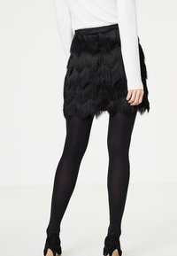 Svart fransad kjol med en texturerad design och lager med vågiga detaljer. Bärs med svarta strumpbyxor och svarta klackskor.