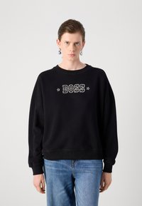 Felpa nera con logo "BOSS" bianco, dotata di collo tondo e polsini a coste, abbinata a jeans azzurri chiari. Design semplice.