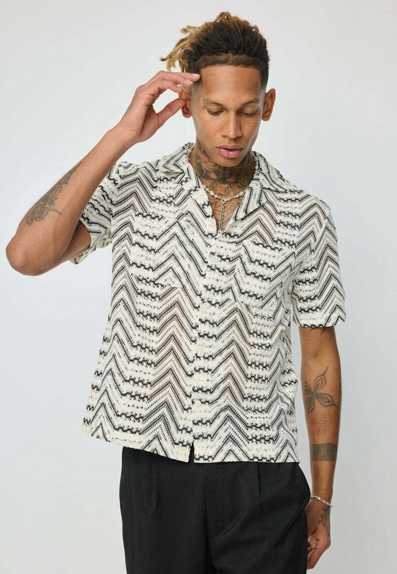 Chemise à manches courtes en tissu léger et transparent, avec un motif zigzag noir et blanc, un devant à boutons et un col.