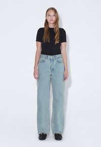 Jeans de tiro alto en azul claro con un diseño de pierna recta, lavado desvaído y costuras visibles. Combinados con una camiseta negra ajustada.