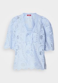 Lichtblauwe blouse met bloemen uitsnijdingen, een golvende zoom en een striklint bij de hals. Korte pofmouwen maken het ontwerp compleet.