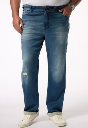 Pantalones jogger de mezclilla en un degradado de azul oscuro a claro, con detalles desgastados, cintura con cordón y puños enrollados, combinados con zapatillas blancas.
