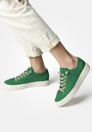Green leather sneakers with round toe, tan laces, and gold-tone eyelets. Set against light-colored rolled-up pants on a neutral background.