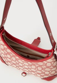 Borsa a mano in pelle rossa e tela con un motivo intrecciato texturizzato, dotata di chiusura con zip e numerosi scomparti interni.