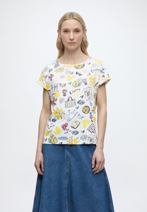 Frau trägt ein weißes Kurzarmhemd mit bunten Lebensmitteln und sommerlichen Skizzen, kombiniert mit einem blauen Jeansrock.