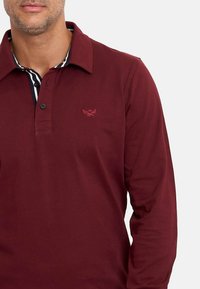 Polo de manga larga burdeos con cuello, que presenta una tapeta de dos botones, logo bordado y detalle de cuello interior a rayas.