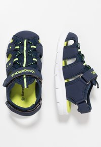 Navy blue sandals with white soles, featuring mesh upper, bright green accents, and adjustable straps for secure fit.