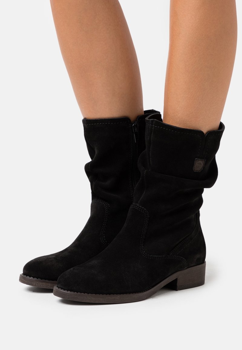 Bottines en suede noir avec un design drapé, dotées d'une fermeture éclair sur le côté, de coutures accentuées et d'un petit talon carré.