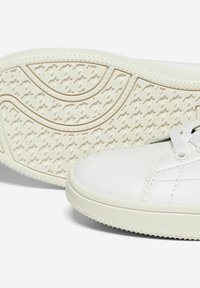 Baskets en cuir blanc avec bout rond, semelle plate et semelle en caoutchouc texturé arborant un motif géométrique. Lacets et coutures visibles.