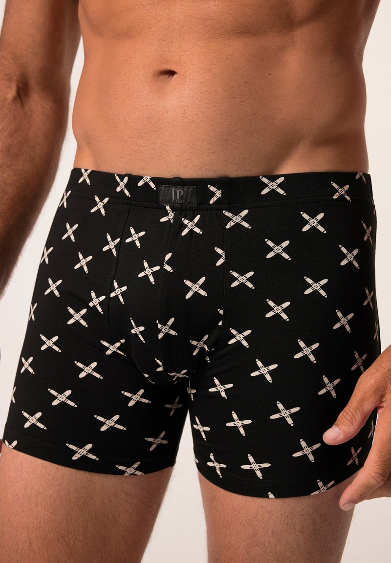 Boxer-culottes noires avec un motif en X blanc répétitif. Fabriquées en tissu doux, elles présentent une taille élastique et un design ajusté.