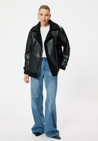 Svart läderjacka med fårskinnskrage, dragkedja fram, och uppvikta ärmar, i kombination med ljusblå vida jeans och en vit topp.