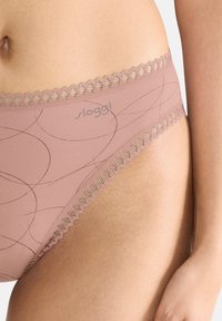 Roze herenonderbroek met een gladde textuur, voorzien van subtiele cirkelpatronen en een decoratieve kanten rand in een lichtere tint. Sloggi-logo zichtbaar.