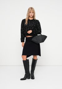 Czarny sweter zdobiony kwiatami, połączony z asymetryczną spódnicą w kolorze czarnym, czarnymi skórzanymi botkami do kolan oraz elegancką czarną torebką.