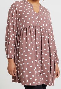 Hnědá blůza s puntíky, dlouhými rukávy, knoflíkovou přední částí a nařaseným pasem. Měkká tkanina s bílými kulatými vzory, pohodlný střih.