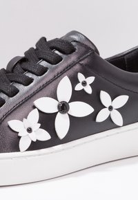 Black leather sneaker with white floral decorations, black accents, round laces, and a white rubber sole. Smooth texture with glossy finish.