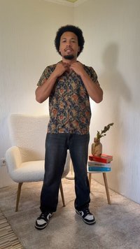 Koszula z krótkim rękawem w wzory kwiatowe w żywych kolorach, zestawiona z ciemnymi dżinsami i czarnymi trampkami.