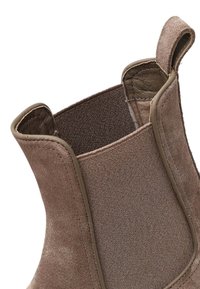 Bottines en suède marron avec panneau en textile, côtés élastiques et languette de traction. Matériau texturé et coutures visibles autour des bords.