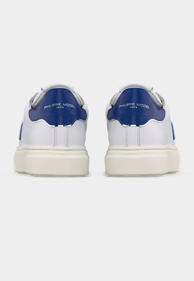 Λευκά αθλητικά παπούτσια με μπλε ταμπελάκι στη φτέρνα με την επιγραφή "Philippe Model Paris", εμφανιζόμενα από πίσω σε απλό λευκό φόντο.