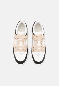 Tenisky s bílou špičkou, béžovým středním dílem a černou zadní částí. Mezi rysy patří perforace, béžové tkaničky a bílá gumová podrážka.