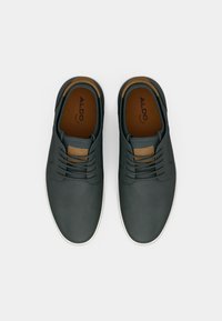 Scarpe grigio scuro con una texture liscia, suola bianca, punta rotonda e un accento in pelle marrone sul linguetta. Stile con lacci e sei occhielli.