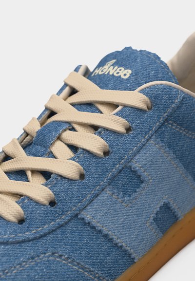 Μπλε τζιν αθλητικό παπούτσι με μπεζ κορδόνια, σόλα από καουτσούκ και το λογότυπο "HGN86" κεντημένο στη γλώσσα.