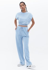 Sudadera recortada de color azul claro con mangas cortas, combinada con pantalones de chándal de pierna ancha a juego que cuentan con una cinturilla elástica y cordón.