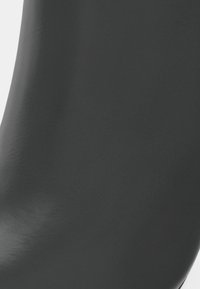 Acercamiento a una superficie de cuero negro suave con sutil textura y pliegues naturales, mostrando la calidad y el acabado del material.