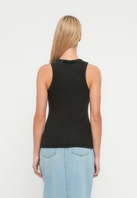 Black ribbed tank top with a round neckline and sleeveless design, featuring a smooth texture and a fitted cut, paired with a light denim skirt.