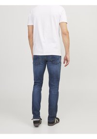 Herrarnas blå denimjeans med smal passform, kontrasterande sömmar och bakfickor. Kombineras med en enkel vit t-shirt och svarta sneakers.